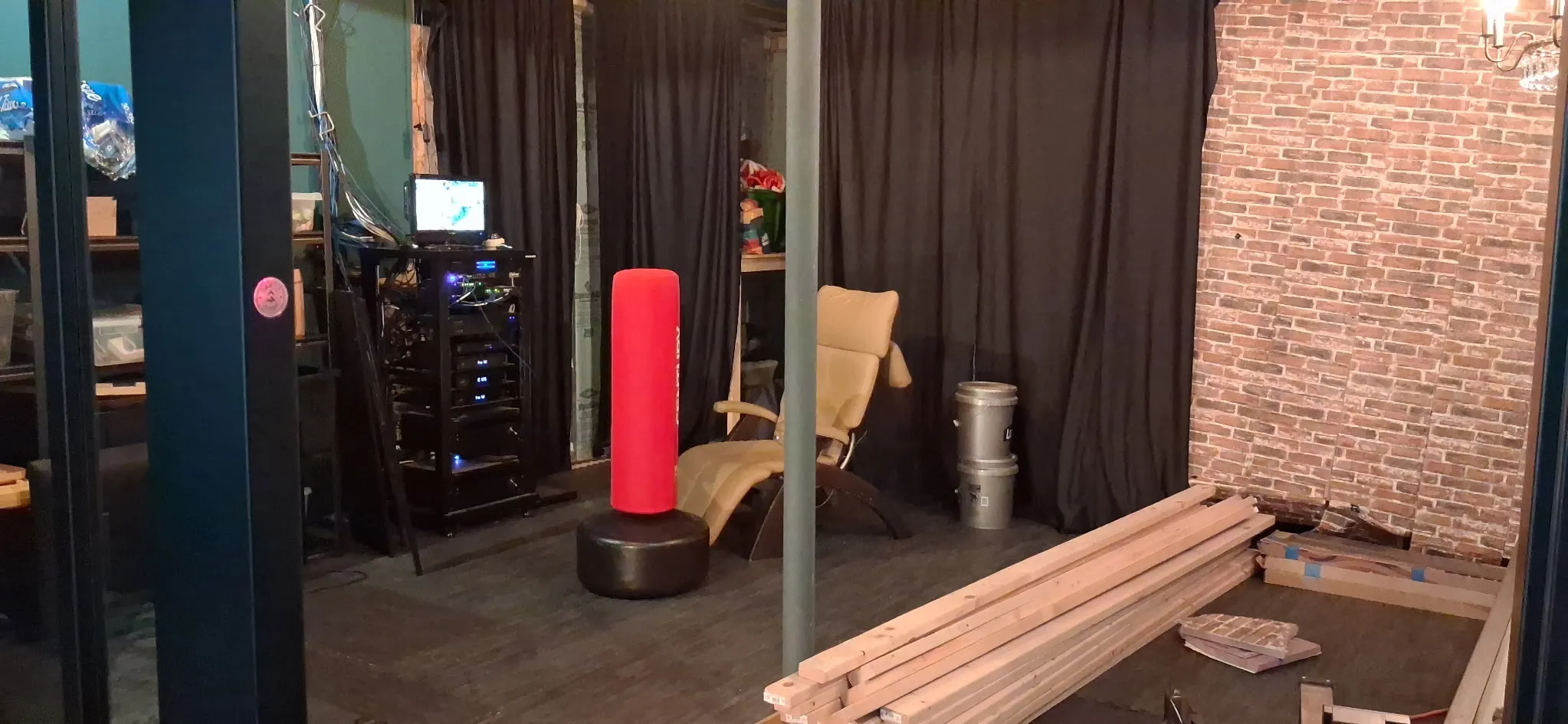 The same basement mid-build, with a brick accent wall going in and framing lumber staged on the floor