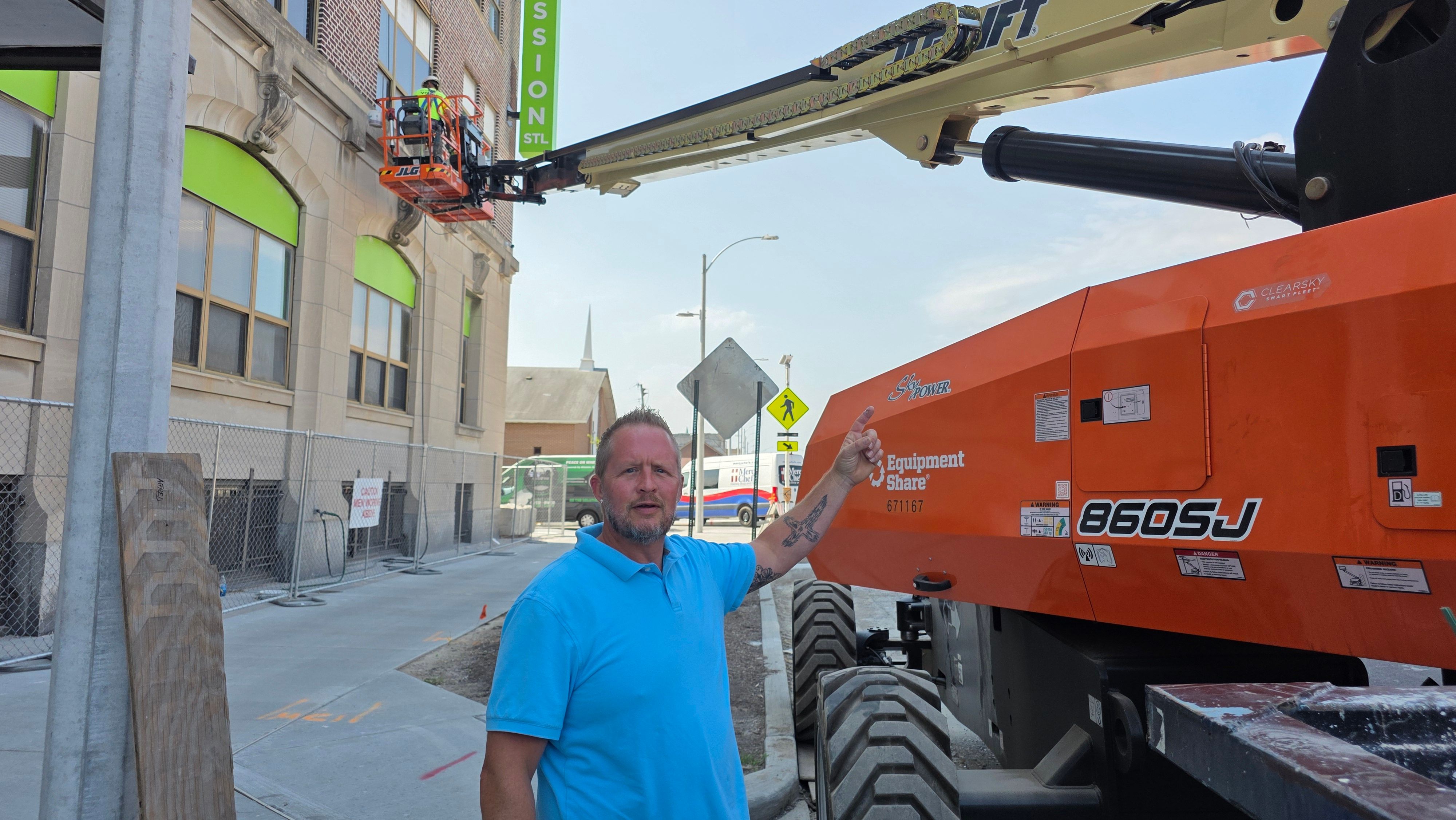 Matt Overmann on a job site pointing up at a boom lift
