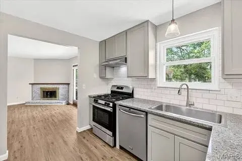 A kitchen with grey shaker cabinets and a white subway tile backsplash running behind the range, around the window and along the granite counter