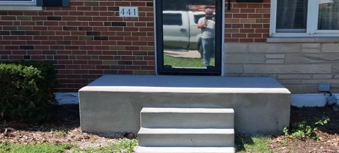 A concrete front stoop and three steps with no handrail of any kind
